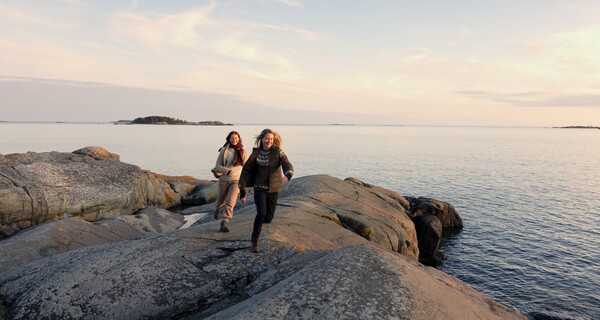 Två kvinnor springer på klippa vid havet